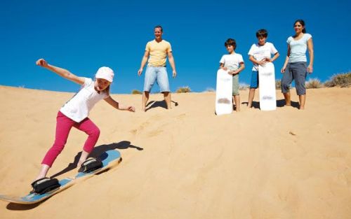 A family watching their daughter ride down a sand dune on a sandboard at Cunnamulla