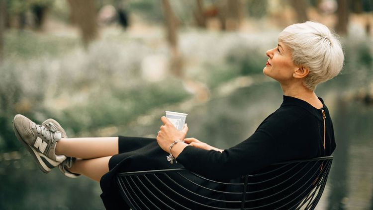 A woman in a black dress sitting in a chair looking gazing wistfully into the distance